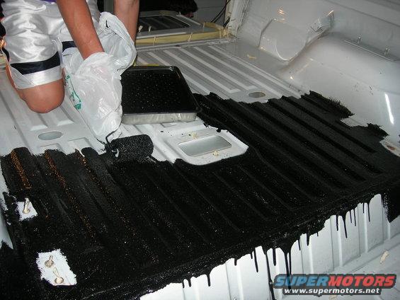 person applying black coating to a white truck bed with a roller