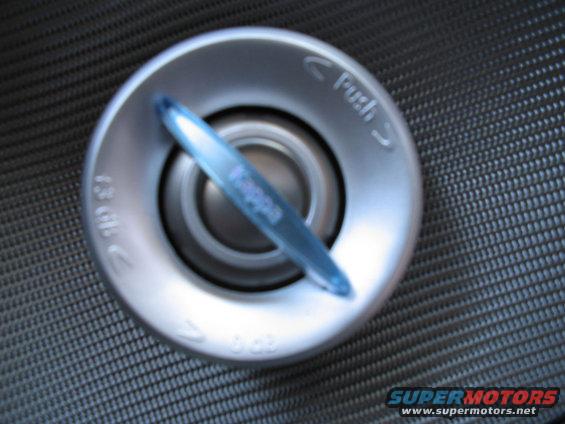 Silver fuel filler cap with blue plastic tab and "Push" text