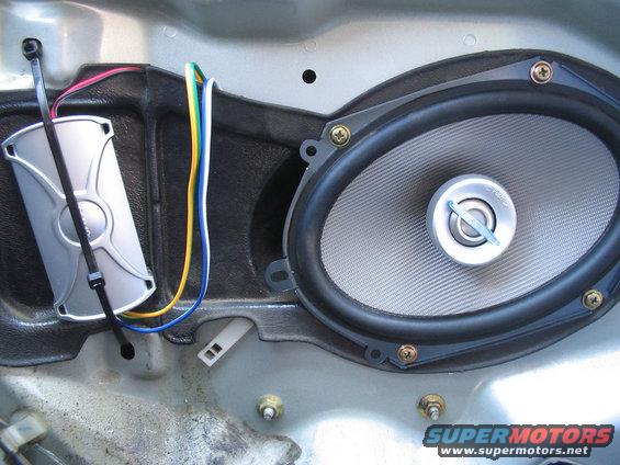 Car door panel removed showing an oval speaker, wiring, and a silver electronic component secured with zip ties