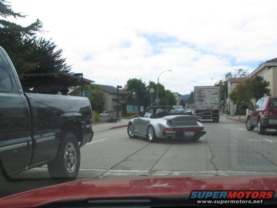 Silver convertible sports car with a rear spoiler driving on a street, next to a black pickup truck