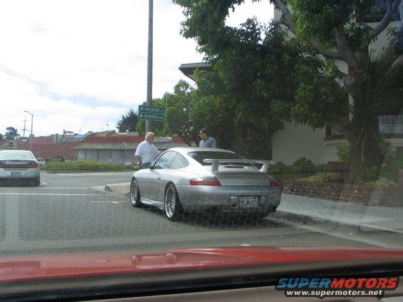 Silver Porsche 911 with a large rear spoiler parked on a street, seen from behind