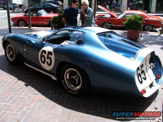 Blue race car with white stripe and number 65 on door and rear. Other cars visible in background