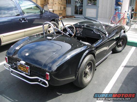 black convertible sports car parked next to a dark minivan, with a bicycle in the background