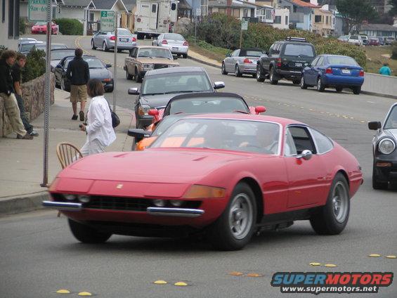 Red Ferrari 365 GTB/4 Daytona coupe driving on a street, front 3/4 view