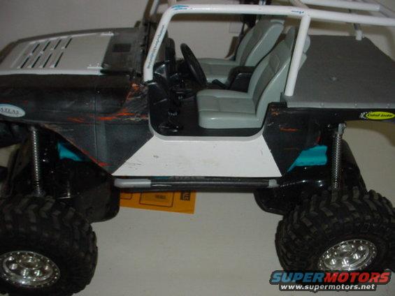 RC crawler vehicle with roll cage, gray seats, and black body with orange scratches