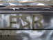 1988 Ford Bronco - A car's rear panel shows spray-painted letters and a website logo, indicating it is a part of a vehicle.