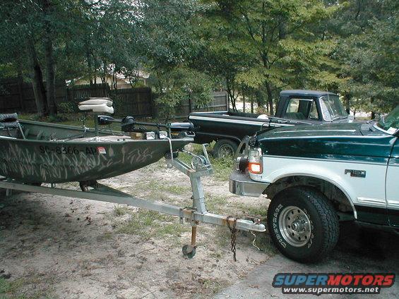 Green and white pickup truck towing a camouflage boat on a trailer. The truck has a "F-150" badge visible