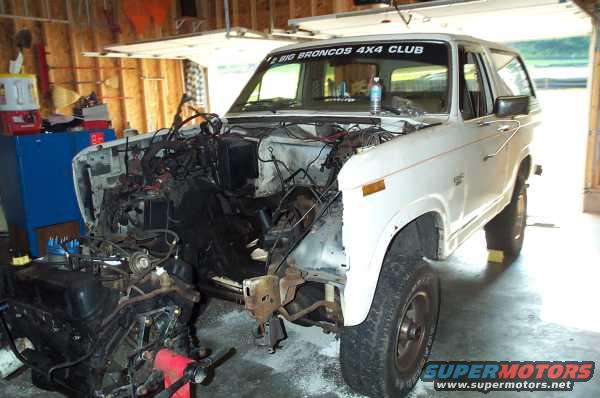 1985 Ford Bronco with engine removed, parked in a garage. Banner on windshield reads 'BIG BRONCOS 4X4 CLUB'