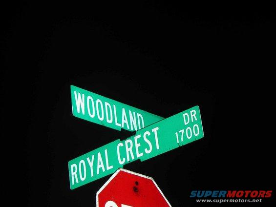 Green street signs for Woodland and Royal Crest DR 1700 against a black background