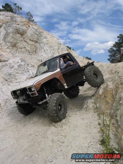 Modified pickup truck with large tires climbing a steep, rocky incline