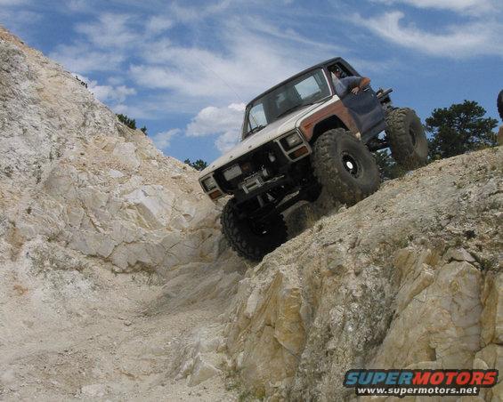 1981 Ford Bronco climbing a steep, rocky hill with large off-road tires