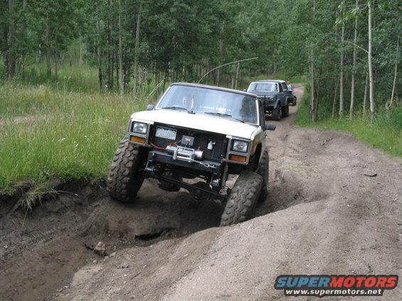 White Jeep Cherokee XJ climbing a dirt embankment, another Jeep behind it