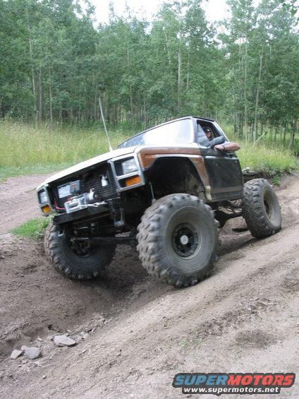 Big tires on a lifted SUV going up a dirt hill, trees in background
