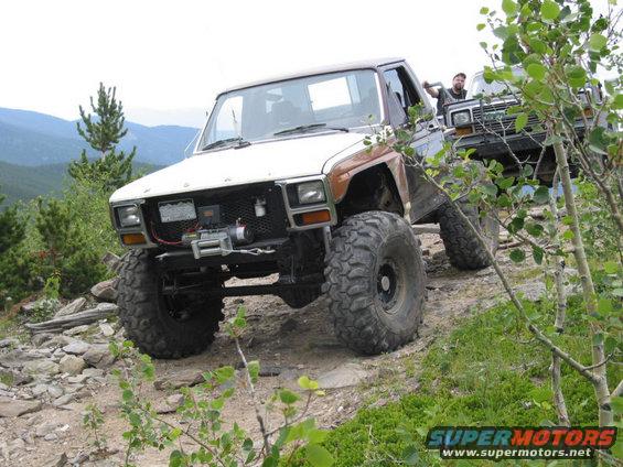 Modified 1980s Ford Bronco with large tires on a rocky trail, another vehicle behind it