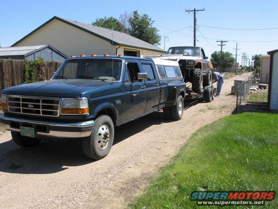 Blue Ford F-350 dually truck towing a lifted, older model truck on a trailer