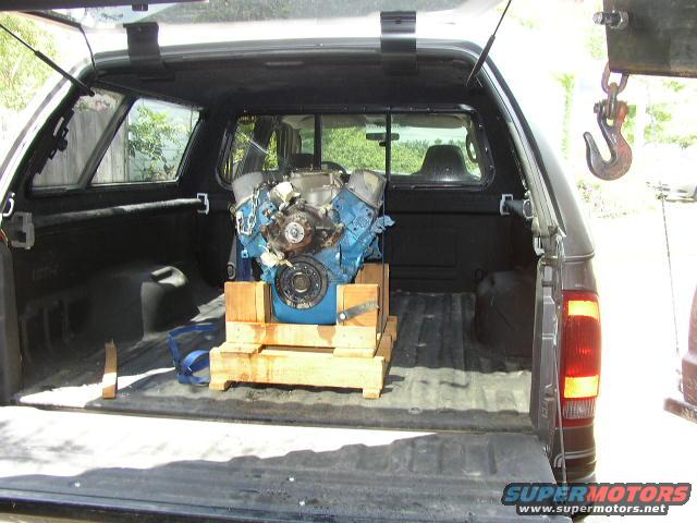 Truck bed with an engine on a wooden pallet, a hook hangs from above
