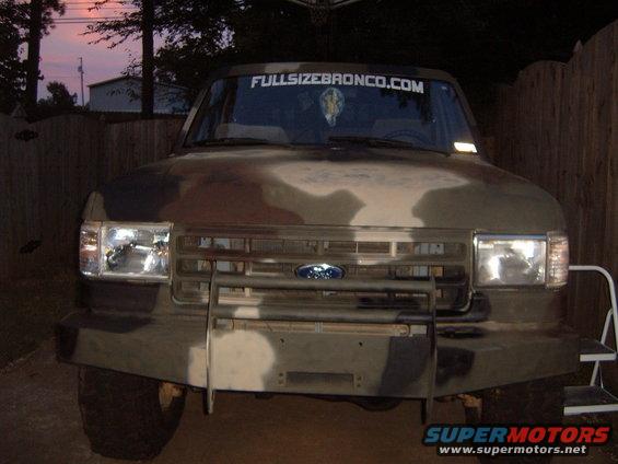 Front view of a Ford Bronco with camouflage paint and a "FULLSIZEBRONCO.COM" banner on the windshield