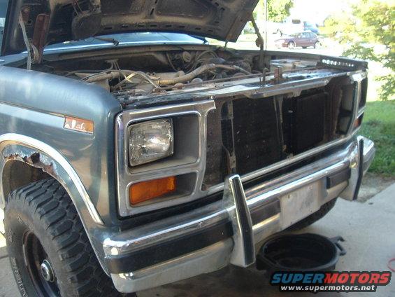 1980 Ford Bronco front end, hood open, showing engine bay. Chrome bumper and grille are visible, with rust on the fender