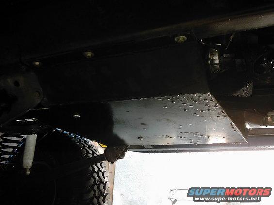 Underbody skid plate with visible bolts and rivets, part of a vehicle's suspension system including a shock absorber and tire
