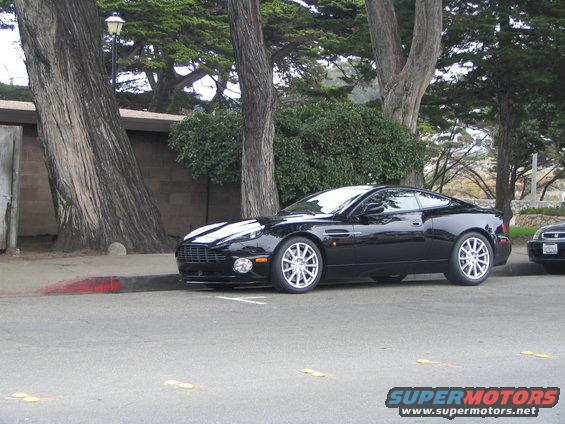 Black Aston Martin coupe parked on street, another car partially visible behind it