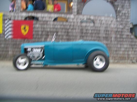 Blue hot rod with exposed engine and chrome wheels, seen from the side