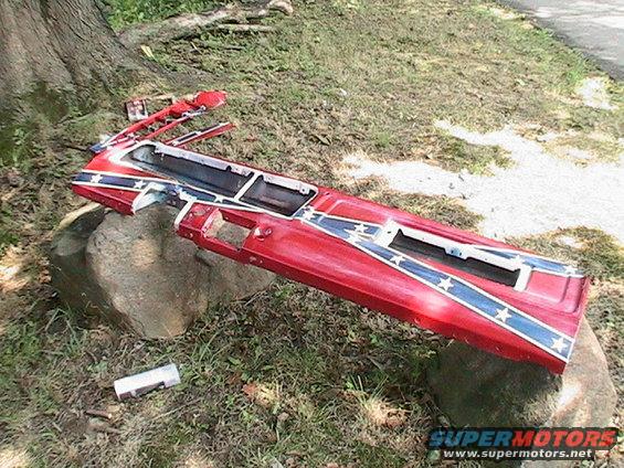 Red car door panel with Confederate flag design, broken and resting on rocks