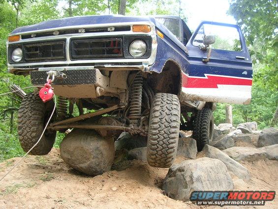 1977 Ford F-150 with blue and red paint on off-road course, front wheel on rock