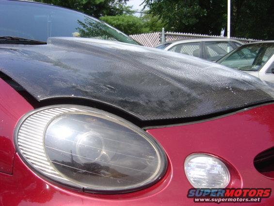 Red car front with aftermarket carbon fiber hood and oval headlight