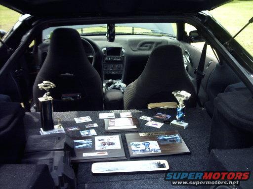Interior of a black car with two bucket seats, trophies, and plaques on display