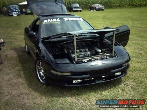 black coupe with hood and trunk open, showing engine. Text on windshield reads 'ANAL PROBE'. Other cars in background