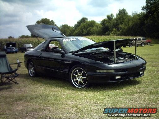 Black 1995 Ford Probe with hood and trunk open, parked on grass with other vehicles in background