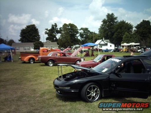 Black sports car with hood and door open, chrome wheels, parked on grass at an outdoor event