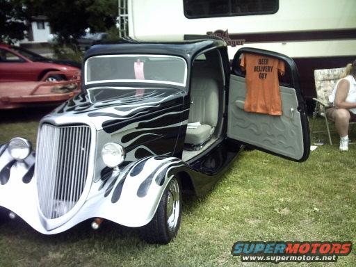 Hot rod with flame paint, open door shows t-shirt that says "BEER DELIVERY GUY". Another car is visible in the background
