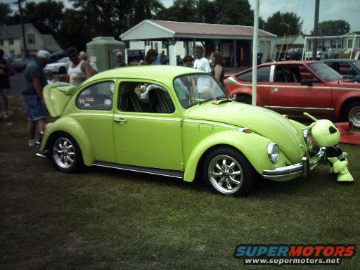 Lime green Volkswagen Beetle with a stuffed alien on the front bumper. A red AMC car is parked behind it