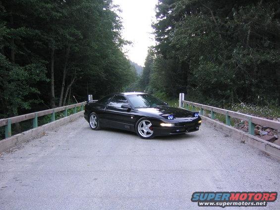 Black 1994 Ford Probe on a bridge with trees in background