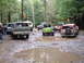 1995 Ford Bronco - Multiple off-road vehicles are gathered in a muddy clearing within a wooded area.
