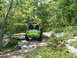 1995 Ford Bronco - A bright green Jeep navigates a rocky path through a dense forest.