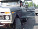 1979 Ford Bronco - A dark-colored pickup truck with its door open, showing a driver inside. Another white truck is visible in the background.