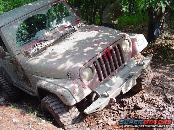 Mud-covered Jeep Wrangler stuck in dirt, front view