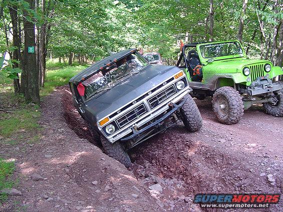 Gray 1978 Ford Bronco tilted in a ditch with a green Jeep nearby