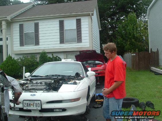 1996 Ford Probe with hood open, engine bay visible, and a person standing nearby. Another red car is behind it