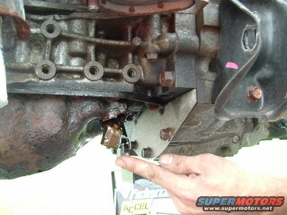Engine oil pan leak with a finger pointing to the damaged area