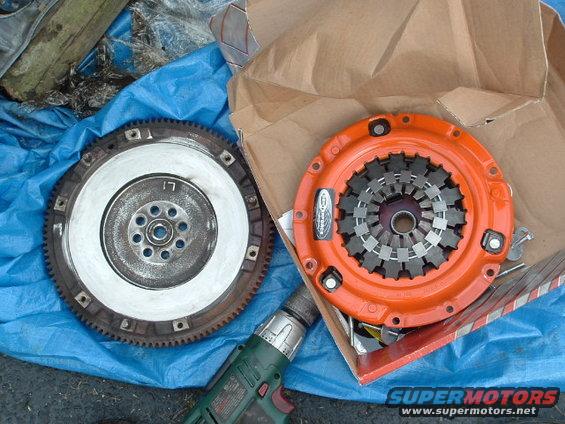 Orange clutch assembly and metal flywheel on blue tarp with drill