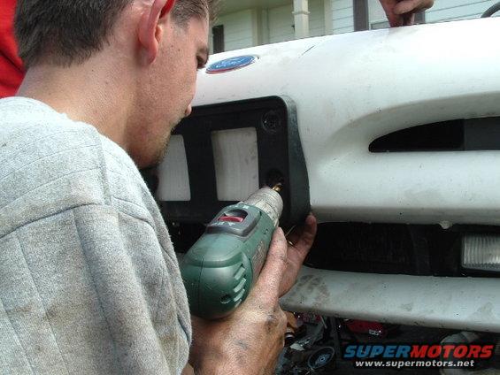 guy drilling into the front grille of a white vehicle, possibly a truck