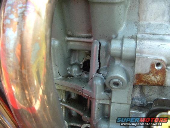 Engine block with large cracks and a hole, showing metallic texture and some rust