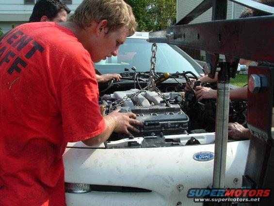 Engine being removed from a white car with a Ford logo