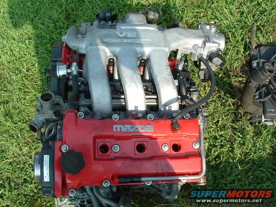 Mazda V6 engine with red valve covers and silver intake manifold, resting on grass