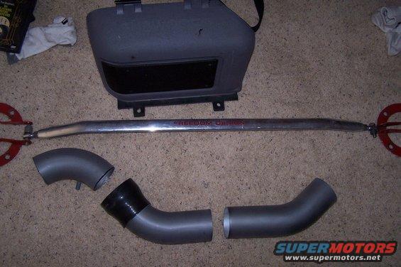 Car strut bar with red mounting plates and intake piping parts on carpet. Text on bar reads 'FREEDOM DESIGN'