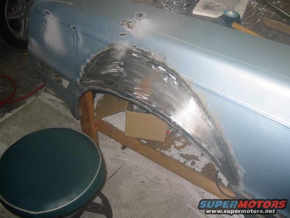 Close-up of a car's rear fender being repaired with metalwork and primer