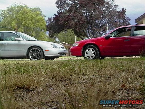 Silver and red sedans parked side-by-side on grass. The silver car is a 1995 Ford Taurus